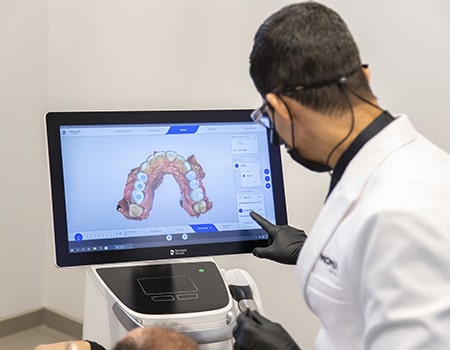 Dr. Carlos using a monitor of a CEREC machine that shows the teeth of a patient